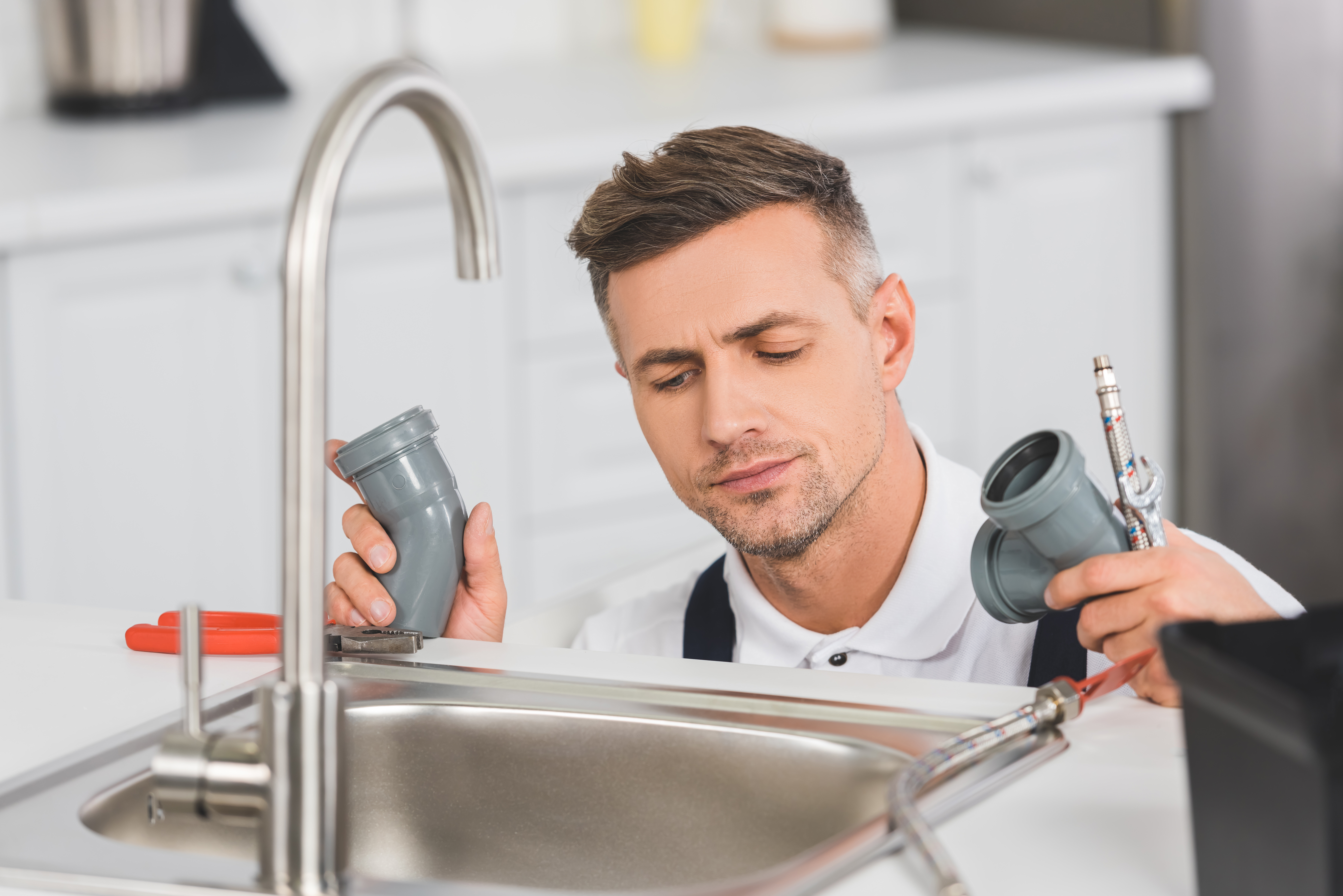 Plombier examinant des tuyaux sous évier cuisine.