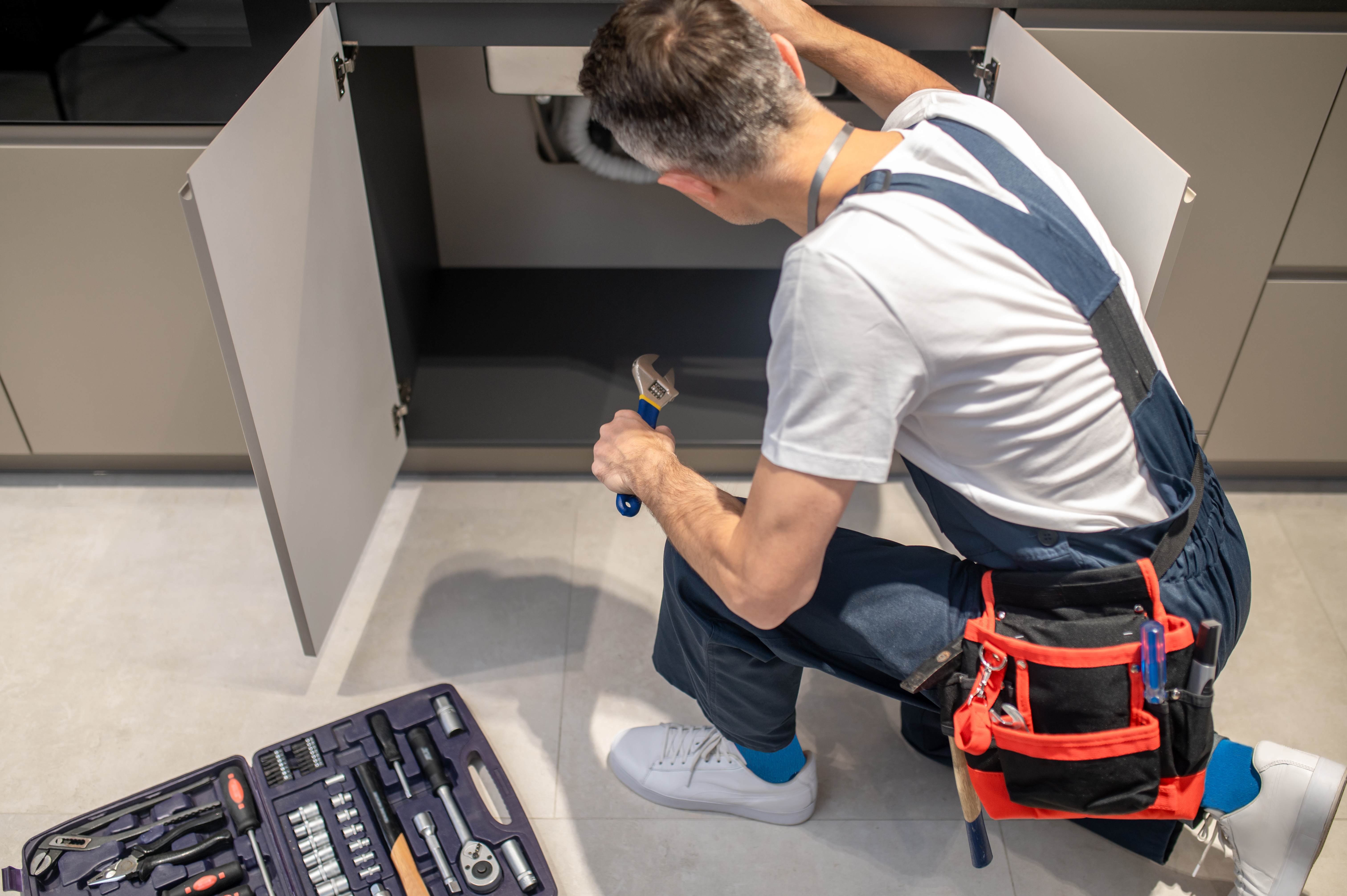 Plombier répare tuyau sous évier avec outils.