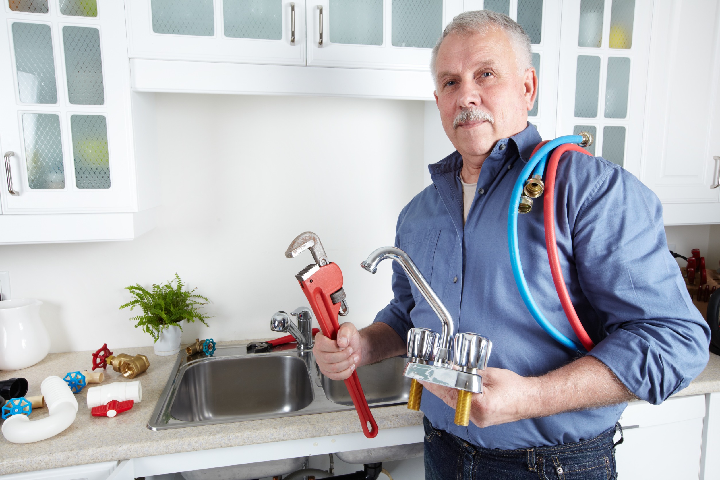 Plombier tenant outils et matériel dans une cuisine.